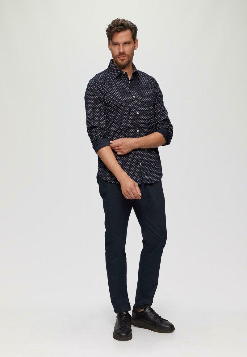 Marineblauwe button-up shirt met witte stippen, opgerolde mouwen, gecombineerd met donkere broeken en zwarte sneakers. Eenvoudig ontwerp, gladde textuur.