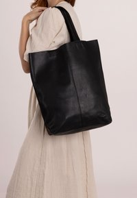 Bolso tote de cuero negro con superficie texturizada, asas trenzadas resistentes y un interior amplio y profundo. Diseño minimalista, sin hardware visible.