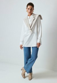 White long-sleeve shirt with a large beige collar and button details, paired with light blue flared jeans and beige heeled boots.