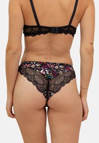 String noir en dentelle avec un motif floral coloré. Dispose de bords en dentelle festonnés et d'un tissu doux pour le confort. Bretelles ajustables.