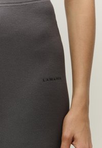 Šedé žebrované legíny s priliehavým strihom, s nenápadným embosovaným logom "LAMANA" blízko pásu. Hladká textúra a pružný materiál.