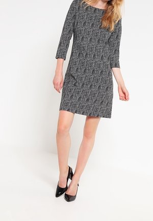 Robe à motifs noir et blanc avec des manches trois-quarts, un buste ajusté et une silhouette droite. Portée avec des chaussures à talons hauts noires.