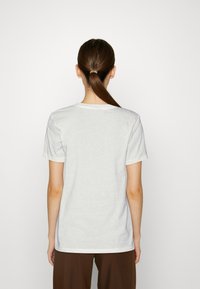 Bílý bavlněný tričko s kulatým výstřihem a krátkými rukávy, s jednoduchým, bezešvým designem bez ozdob nebo vzorů.