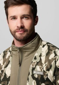Fleecejacke mit Reißverschluss, ausgestattet mit einem Camouflage-Muster in Grüntönen und Brauntönen, und einem einfarbigen olivgrünen Kragen sowie Logo.