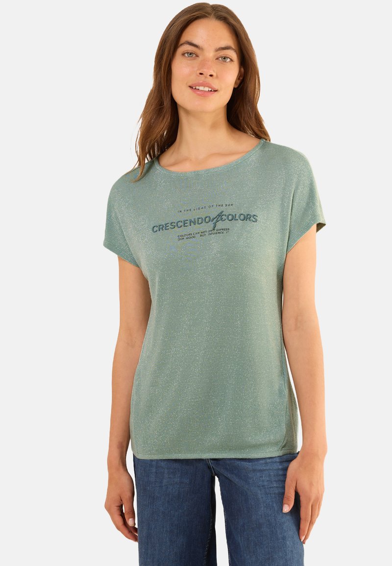 T-shirt vert clair à manches courtes avec un col arrondi et un éclat métallique. Présente un slogan imprimé en bleu foncé sur le devant.