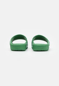 Gröna flexibla sandaler med öppen häl, texturerade sidor och horisontella ränder, tillverkade av lätt material.