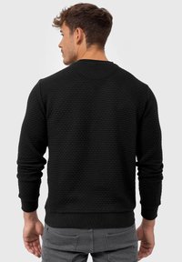 Sudadera negra con textura, cuello redondo, puños y dobladillo de canalé. Presenta un patrón en relieve y un diseño de corte relajado.