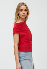 Czerwony dopasowany top o fakturowanej tkaninie, z off-the-shoulder, krótkie rękawy, oraz marszczone detale po bokach, połączony z dżinsową spódnicą.