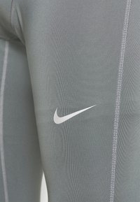 Leggings de sport gris avec une texture lisse, dotés de coutures plates et d'un petit logo Nike swoosh blanc sur la cuisse.