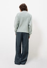 �Übergroßer hellgrüner Strickpullover mit gerippter Textur, kombiniert mit locker sitzenden, dunkelgrauen Hosen, beide Rückansicht vor einem weißen Hintergrund.