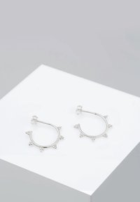 Boucles d'oreilles anneaux en argent avec de petits picots triangulaires espacés uniformément tout autour du bord extérieur, présentées sur une surface blanche.