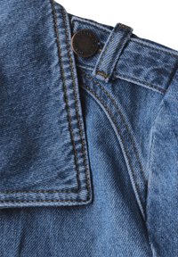 Jeansjacka avsnitt med krage, metalldetalj och kontrasterande gul sömnad på ljusblått tyg, som visar textur och designfunktioner.