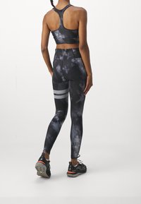 Svart och grå tie-dye sport-bh i kombination med högmidjade tights med en strukturerad grå rand. Träningsskor fulländar looken.