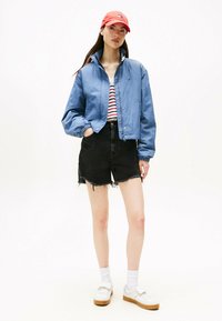 Jasnoniebieska, wodoodporna kurtka bomberka z kołnierzem stojącym i elastycznymi mankietami; czarne szorty dżinsowe z postrzępionym dołem; białe trampki; czerwona czapka.