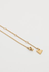 Gouden ketting met een gedraaide ontwerp, een kreeftenhaak en een driehoekige hanger met de gegraveerde merknaam.