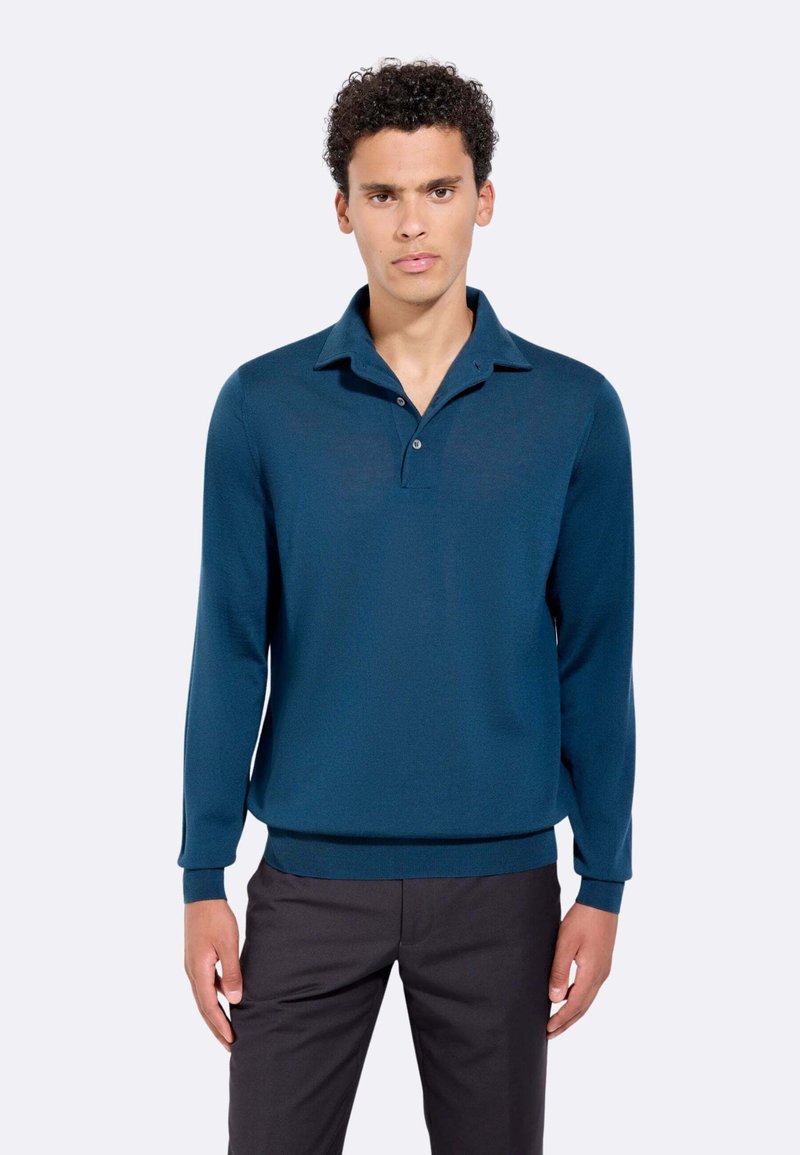 Maglione dolce di colore blu scuro con colletto, maniche lunghe e due bottoni. Tessuto testurizzato con una finitura liscia; abbinato a pantaloni scuri.