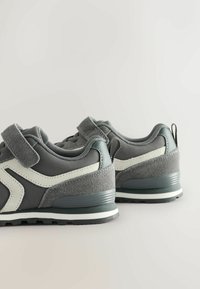 Gray athletic shoes with a textured suede and synthetic upper, featuring a green accent, adjustable strap, and a cushioned sole.