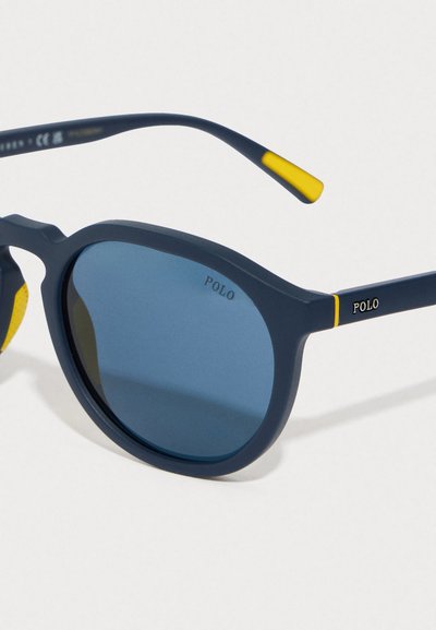 Ochelari de soare bleumarin cu rame rotunde, lentile cu nuanță albastră și finisaj mat. Prezintă accente galbene pe brațe și branding "POLO".