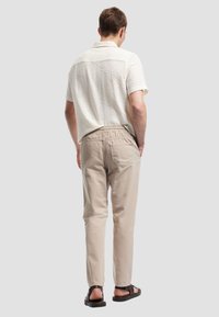 Heren overhemd met korte mouwen, ivoorkleurig patroon en een kraag, gecombineerd met beige elastische broeken en bruine sandalen. Schoon, modern ontwerp.