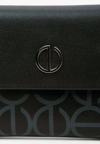 Zwarte leren portemonnee met een geperforeerd cirkelpatroon, voorzien van een zilver metalen logo-sluiting. Glad van textuur en een slank ontwerp.
