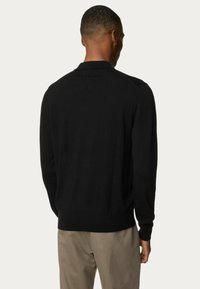 Sort sweater med en glat tekstur, ribbede kanter og manchetter samt en klassisk krave. Udsigt fra ryggen, parret med beige bukser.