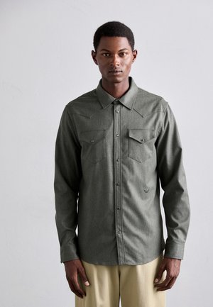 Long-sleeve dark green shirt in a textured fabric with a button-up front, two chest pockets, and pointed collar details.