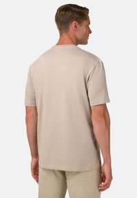 Svetlo béžové tričko s krátkym rukávom a voľným strihom. Mäkka bavlnená tkanina, jednoduchý dizajn a na zadnej strane sú žiadne viditeľné vzory alebo grafika.