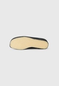 Talpă de pantof neagră cu o suprafață texturată, având un interior de un bej deschis, pufos și o margine exterioară netedă. Formă rotundă, design minimalist.