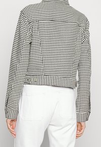 Černobíle kostkovaná zkrácená bunda s kovovými knoflíky, těsně střižená, s dlouhými rukávy. Texturovaná tkanina, podrobné švy.