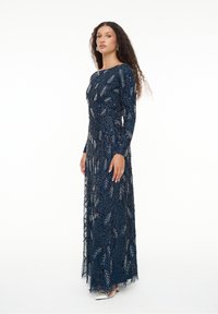 Langärmeliges, bodenlanges Kleid in Marineblau mit filigranen silbernen Blattmustern und Perlenverzierungen, versehen mit einem durchsichtigen Überzug und figurbetontem Schnitt.