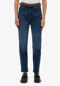 Jeans de mezclilla azul oscuro con cintura alta, pierna recta, cinco bolsillos y un cinturón de cuero trenzado marrón. Combinados con zapatos negros.