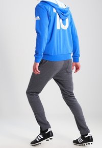 Sweat à capuche bleu avec des rayures blanches et le numéro 10 dans le dos, accompagné d'un pantalon de jogging gris fuselé et de chaussures de soccer noires avec des accents blancs.