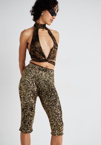 Haut halter brun à motifs avec un décolleté plongeant, associé à un pantalon capri en sequins dorés ajustés, mettant en valeur la texture et l'éclat.