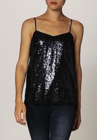 Svart glittrande camisole med tunna band, med en blank, texturerad yta och en V-ringning. Perfekt för lager-på-lager-outfits eller kvällskläder.