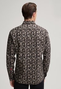 Camicetta a maniche lunghe con sfondo nero e un motivo astratto color crema. Tessuto morbido con colletto a bottoni e dettagli ai polsini.
