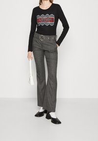 Schwarzes Langarmshirt mit rotem und weißem Grafikdesign, graue karierte High-Waist-Hosen mit einem Gürtel und runder Schnalle sowie schwarze Blockabsatzschuhe.