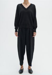 Pull noir à col en V avec manches longues, coupe décontractée, associé à un pantalon noir ample et des chaussures plates noires. Tissu lisse et lignes épurées.