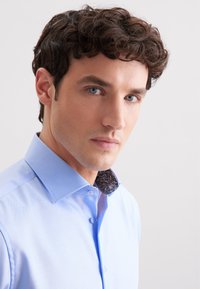 Lichtblauw shirt met een patroon op de donkere kraag, met knoopsluiting aan de voorkant en lange mouwen. Glad textuur, op maat gesneden pasvorm.