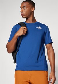 Ανδρικό κοντομάνικο μπλουζάκι σε έντονο μπλε, φτιαγμένο από μαλακό ύφασμα. Διαθέτει λογότυπο στο στήθος και συνδυάζεται με πορτοκαλί σορτς.