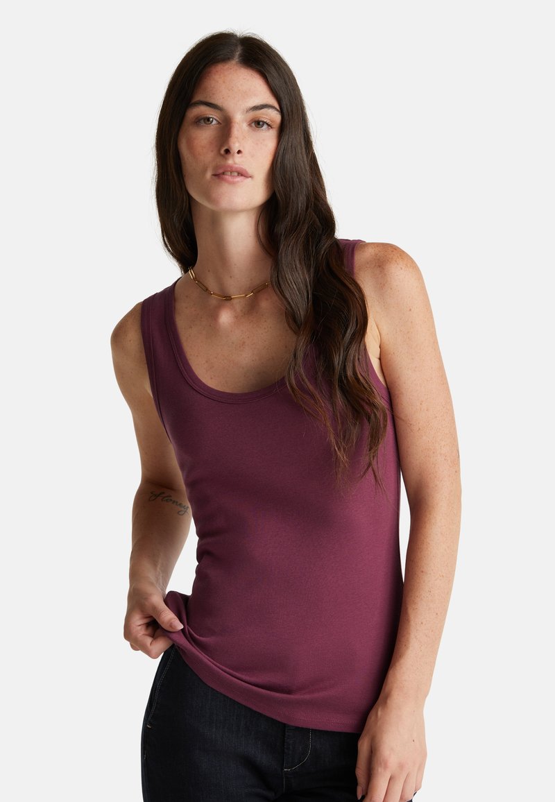 Bordeaux mouwloze tanktop van gladde stof met een ronde hals en een aansluitend ontwerp, gecombineerd met donkere jeans.