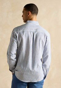 Svītrota zila un balta garām piedurknēm krekls ar pogājamu apkakli un divām pogām aizmugurē, izgatavots no faktūras auduma.