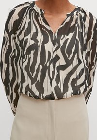 Blouse imprimée en tissu léger. Présente un motif abstrait noir et crème, un décolleté en V et des détails plissés aux épaules.