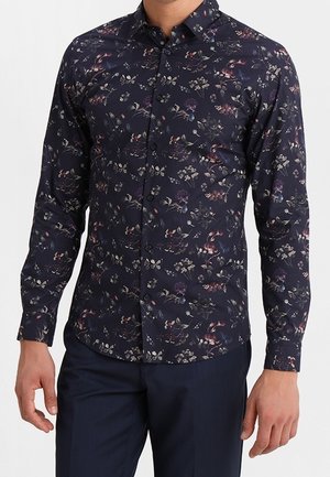 Chemise à manches longues en marine foncé avec un motif floral multicolore. Présente un col à boutons et une coupe ajustée.
