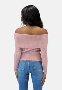Schulterfreier, gerippter Strickpullover in Hellrosa mit langen Ärmeln und taillierter Silhouette, kombiniert mit blauen hochgeschnittenen Jeans.