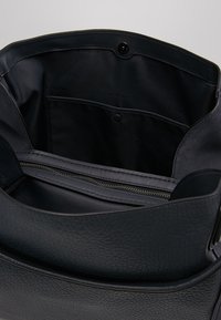 Czarna skórzana torebka o gładkiej fakturze, wyposażona w wewnętrzną kieszeń na zamek i zapięcie na guzik. Wyściełana czarną tkaniną, z wieloma przegródkami.