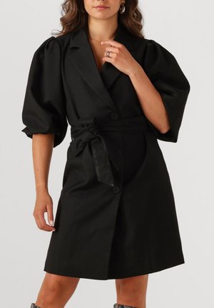 Zwart kort jurkje met poffende mouwen, een ceintuur in de taille en een geknipte kraag. Voorzien van knoopsluitingen en een gladde textuur.