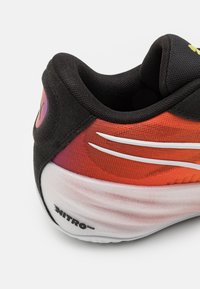 Sort og orange atletiksko-sektion med hvide striber. Har en struktureret sort overdel og en glat hvid sål med "NITRO" logo.