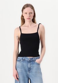 Svart ribbet tank topp med tynne stropper, firkantet utringing, og en tettsittende design, sammen med lyseblå løstsittende jeans.
