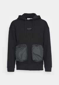 Svart hettegenser laget av bomull, med to store grå glidelås-lommer. Inkluderer en brodert svart logo på forsiden. Justerbar snor for hetten.