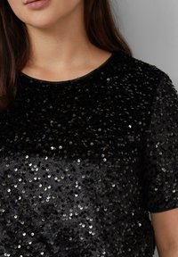 Zwarte korte mouwen top bedekt met platte zwarte en zilveren pailletten, met een ronde halslijn en een gladde stoftextuur.